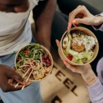 Dwóch mężczyzn trzyma miski z sałatką i makaronem jako zdrowy posiłek