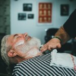 Fryzjer nakłada krem do golenia na brodę dorosłego mężczyzny w barberze