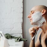 Łysy mężczyzna nakłada piankę i goli szyję maszynką w łazience