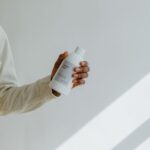 Męska dłoń trzyma minimalistyczną butelkę kosmetyku na jasnym tle